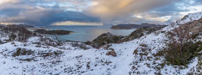 impressive, changing weather moods on the fjord between steep, snow-covered mountains around the island Kvaloya in Troms, Norway. Panorama with sea, dark clouds on the sky and snowy mountains