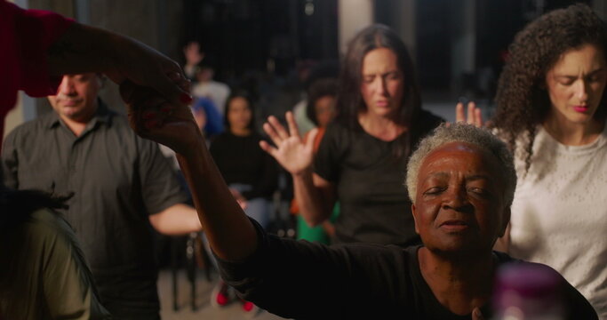 Elderly woman holding hands with spiritual leader during prayer in church, expression of faith and connection, diverse congregation praying in unity in the background