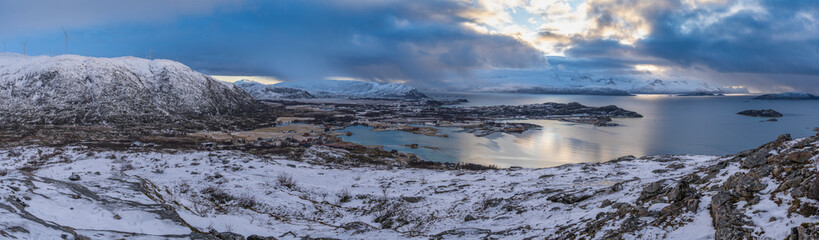 impressive, changing weather moods on the fjord between steep, snow-covered mountains around the island Kvaloya in Troms, Norway. Panorama with sea, dark clouds on the sky and snowy mountains