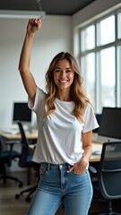 Accelerate action. Stay strong.  A woman in a casual t-shirt standing in a modern office environment, her arm raised in a fist, surrounded by computers. She is smiling and she is happy