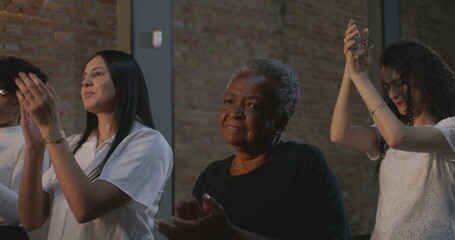 Close-up of diverse group clapping hands during spiritual gathering, elderly woman in foreground with deep focus, symbolic of faith and community connection