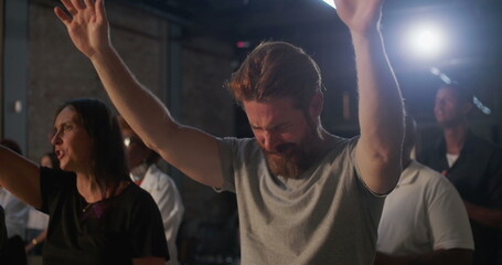 Obraz premium Diverse group in deep prayer, man with clasped hands in foreground showing intense devotion, surrounded by people worshiping in a spiritual gathering