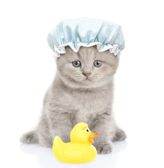 Funny kitten with tiny shower cap on it head sits in front view with rubber duck. isolated on white background