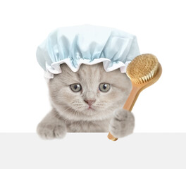 Cute kitten wearing shower cap looks above blank white banner and holds shower brush. isolated on white background
