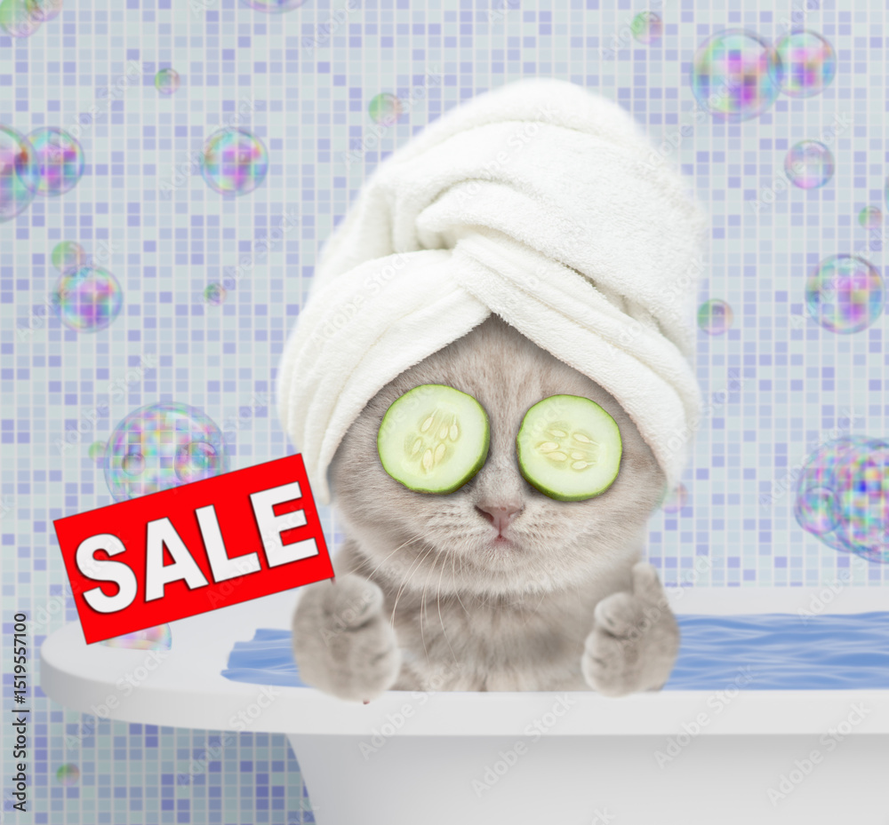 Poster funny kitten with towel on it head and with slices of cucumber on it eyes takes a bath at home, show