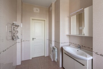 Neutral bathroom with tile walls, white door, vanity, and heated towel rack. Clean and simple design