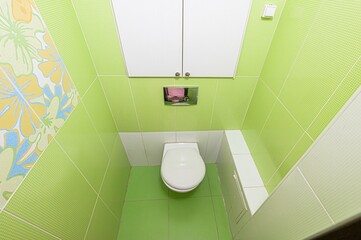 compact, tiled bathroom featuring a white toilet and green, patterned walls