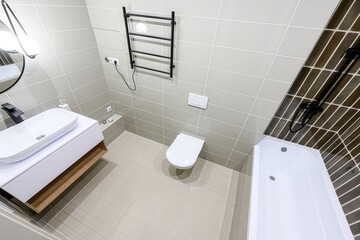 modern bathroom featuring a white sink, toilet, and tub. Gray and brown tiles cover the walls. Black fixtures like a towel rack and shower head add a stylish touch