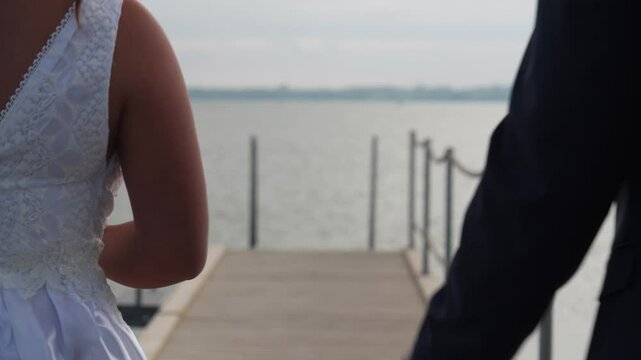 Freshly married couple walk into frame and hold hands, no faces