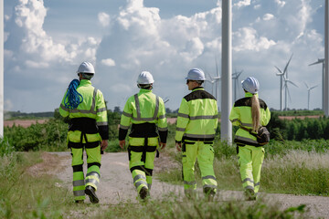 Maintenance engineer team standing at windmills at wind turbine farm. Group of people wear safety...