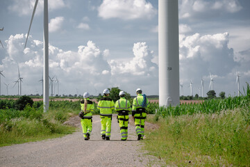 Maintenance engineer team standing at windmills at wind turbine farm. Group of people wear safety...