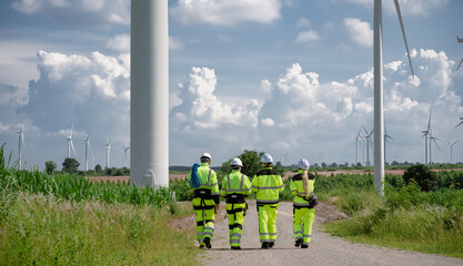 Maintenance engineer team standing at windmills at wind turbine farm. Group of people wear safety...