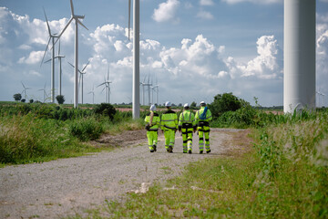 Maintenance engineer team standing at windmills at wind turbine farm. Group of people wear safety...