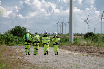 Maintenance engineer team standing at windmills at wind turbine farm. Group of people wear safety...