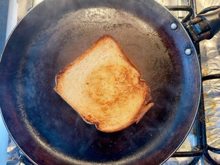 Uma fatia de pão perfeitamente tostada, dourada e estaladiça, numa frigideira quente com vapor visível. Conceito de pequeno-almoço simples, comida caseira e o dia a dia na cozinha.