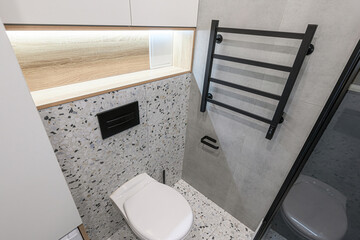 well-lit bathroom features a toilet, black towel rack, terrazzo and gray tiles, and built-in...