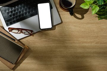 Creative desk including laptop, mobile phone with blank screen, and planner in natural lighting.