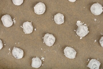Powdered sugar-dusted chocolate crinkle cookies are arranged on a light brown baking sheet, ready...