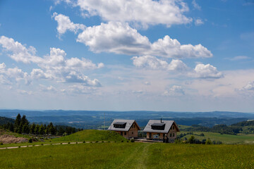 Wooden cottages in scenic mountain meadow under a blue sky with panoramic view of Czech countryside