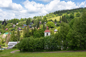 Fototapeta premium View of mountain cottage settlement and old church from grassy ski slope during summer off-season
