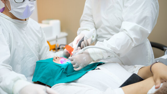 Close-up view of dentist and assistant using curing light tools during a restorative dental treatment on a patient.