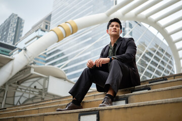 Thoughtful businessman in a suit sitting on steps in business district with a determined expression.