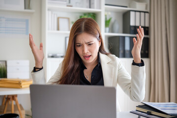 Female office worker raises hands in disbelief while looking at laptop, showing surprise or frustration at unexpected work issue.