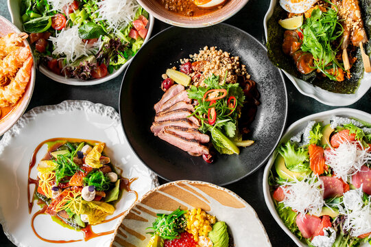 A vibrant assortment of gourmet dishes, including salads, grilled meats, seafood, and colorful garnishes, artfully presented on various plates, showcasing a diverse and appetizing culinary spread.