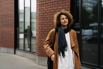 Obraz premium Stylish woman with curly hair walking in the city wearing a brown coat and jeans