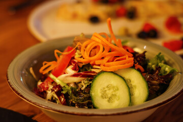 Fresh mixed salad with spiral carrots, cucumber slices, radicchio, and lettuce in a rustic ceramic bowl. Healthy and colorful vegetarian meal served in a restaurant setting.