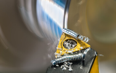 Closeup of lathe tool bit with metal shavings curled up spiral at turning rotating workpiece. Sharp...