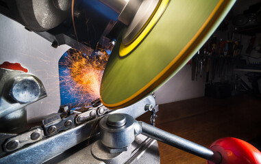 Closeup of chainsaw chain sharpening with rotating disc of grinder machine. Sharp blade of wheel with hot flying sparks at grinding steel tooth edge of cutting tool by professional electric sharpener.