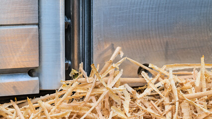 Closeup a wooden shavings pile and metal plane part in background. Detail a sharp steel blade of iron and gray aluminum sole of planing tool with woodwork waste pile of long thin rolled up wood swarf.