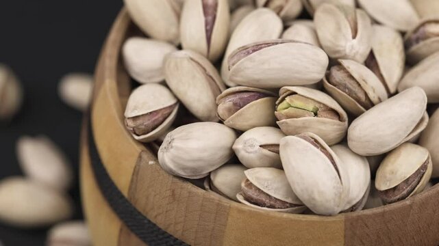 Heap of tasty pistachio nuts in the bowl on dark background.