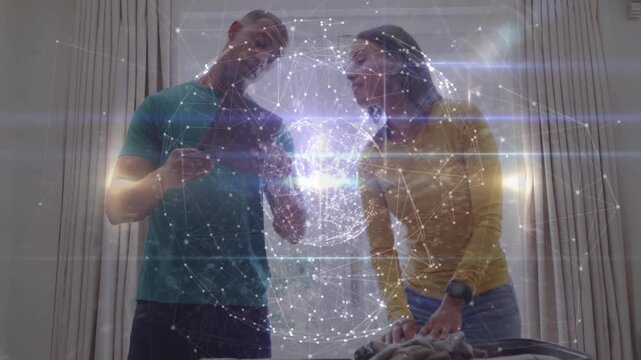 Couple tapping smartphone and projecting technology hologram globe arranging clothes into suitcase - Powered by Adobe