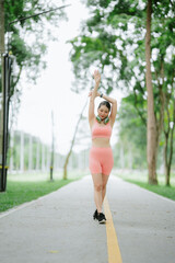 Beautiful Asian woman is exercising and running alone in a village park, happy and smiling in the morning.