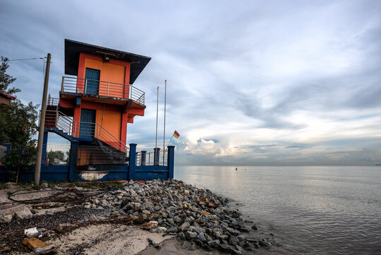 Coastal Guard Tower at Pantai Kelanang, Banting, Malaysia. A striking orange coastal guard tower on the edge of beach, overlooking calm waters under a cloudy sky.
