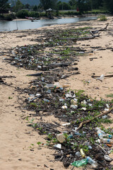 Polluted Beach with Plastic Waste and Debris. A sandy beach covered with scattered plastic bottles, waste, wood debris, and vegetation.