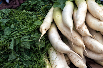 Fresh White Radish and Leafy Greens at Market Stall - A close-up image of fresh white radishes (daikon) displayed alongside leafy green vegetables