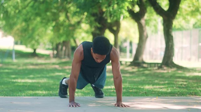 Athletic African American man training burpee movement, captured dynamically in a scenic outdoor park.