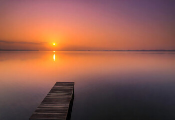 Obraz premium Serene sunset over a calm lake with wooden pier and beautiful reflections