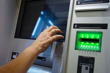 Person operating ATM touchscreen. The interface includes a card reader with glowing green lights and German language labels.