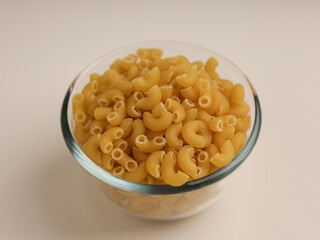 Elbow macaroni in glass bowl, isolated on white