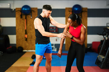Personal trainer examining injured arm of female client during workout in gym