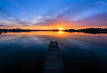 Obraz premium Peaceful sunset over serene lake with wooden pier and breathtaking sky reflections
