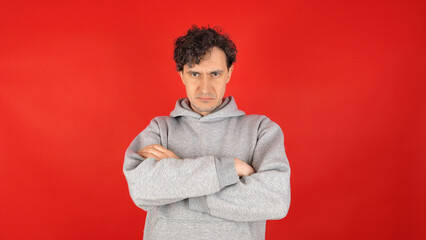 sad, sullen, offended young adult curly man in gray hoodie crosses arms over chest and shakes head...