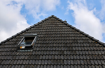 Dark gray roof tiles covering house with skylight and cloudy blue sky