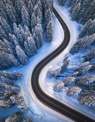 Curvy road in snow covered forest, top down aerial view