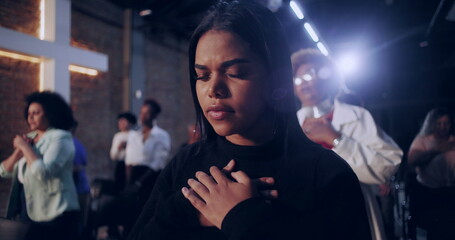 Group of women in prayer inside a church, each with hands over their hearts, expressing faith and devotion, with a glowing cross and brick wall in the background