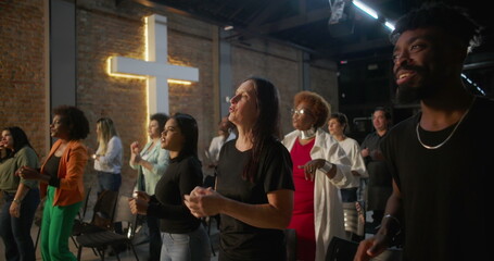 Diverse group of people clapping and smiling during worship in a church, glowing cross in background, expressions of joy, unity, and spiritual connection